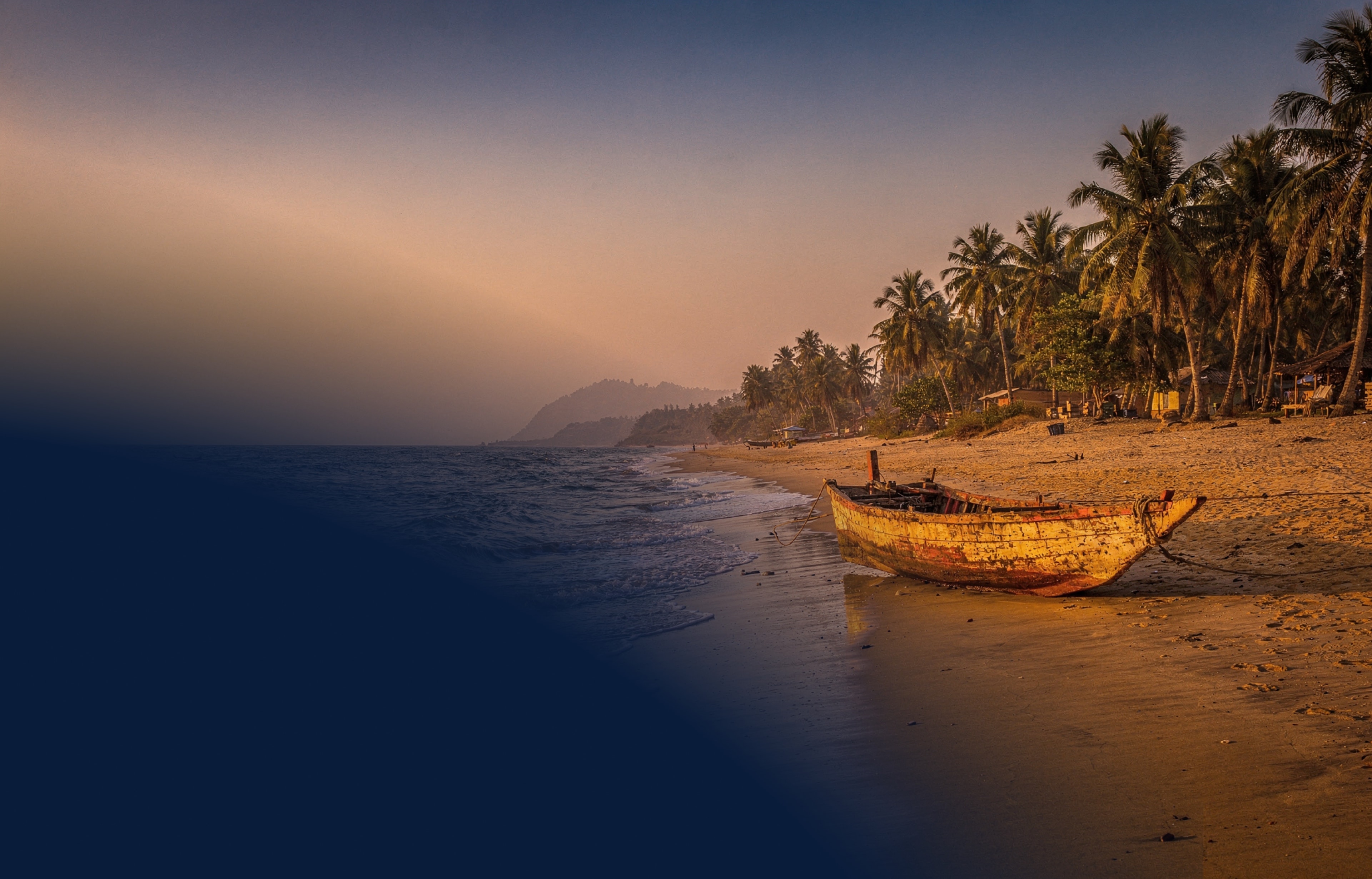 Ghana's coastline at golden hour — wooden fishing canoe pulled onto warm sand with palm trees and distant headland against a sunset sky